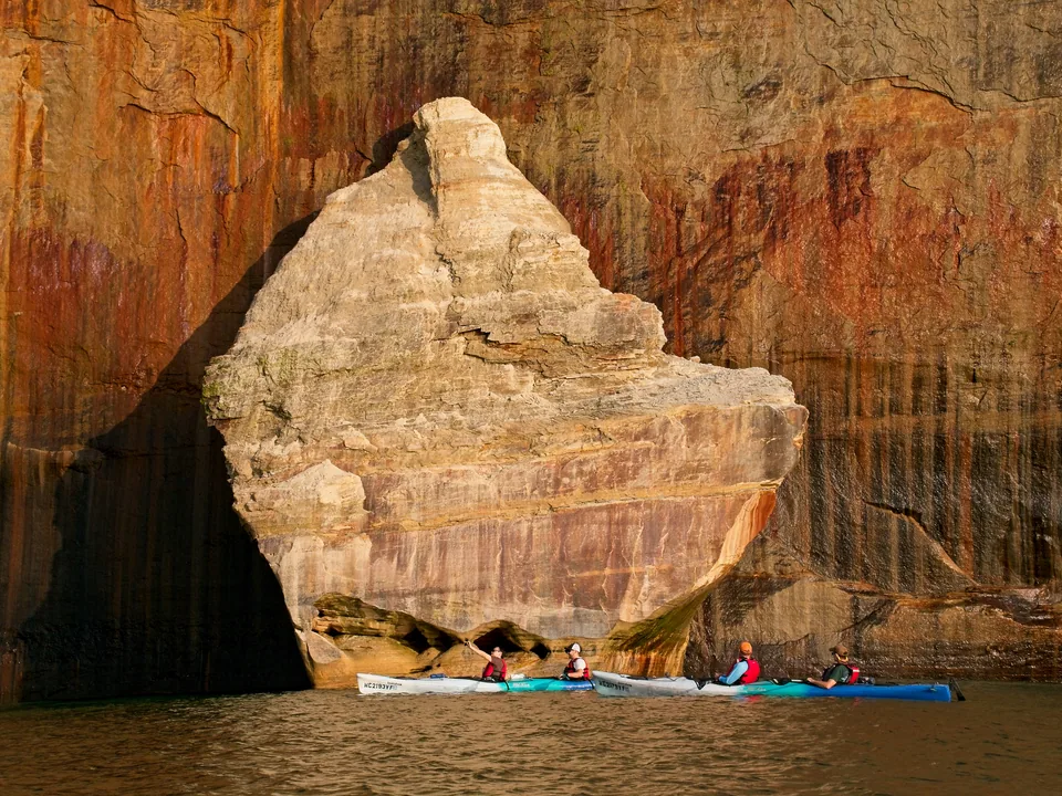 The tour gathers beneath a monumental freestanding slice of Pictured Rocks geology.